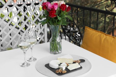 Beautiful roses, glasses of wine and snacks on white table at balcony