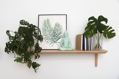 Photo of Ceramic Buddha sculpture with burning candle and decor on wooden shelf indoors. Interior elements