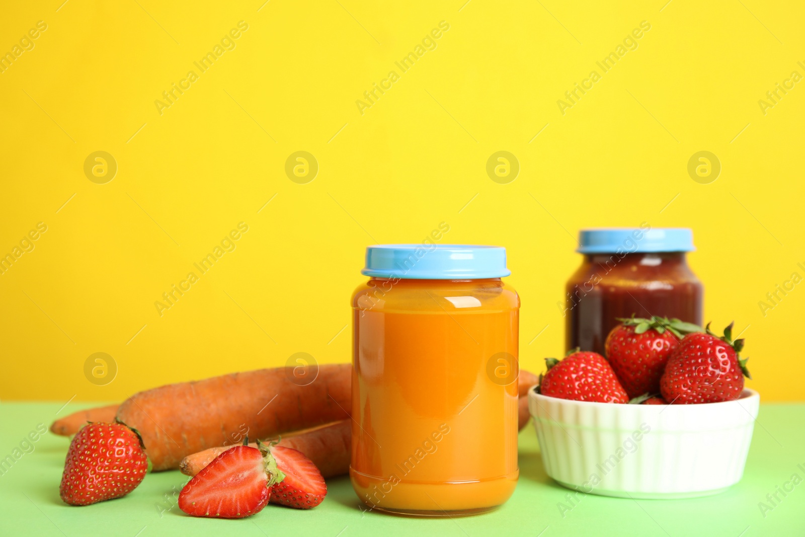 Photo of Jars with baby food and fresh ingredients on green table against yellow background