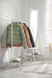 Different warm jackets on rack in stylish room interior