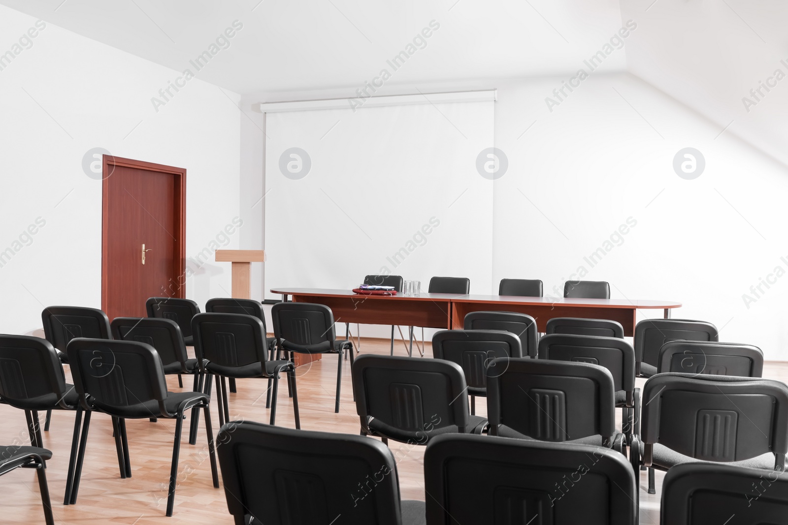 Photo of Empty conference room with projection screen, wooden table and many chairs