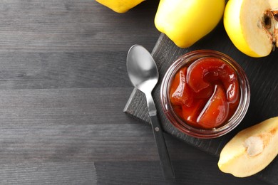 Photo of Quince jam in glass jar, spoon and fresh raw fruits on grey wooden table, flat lay. Space for text