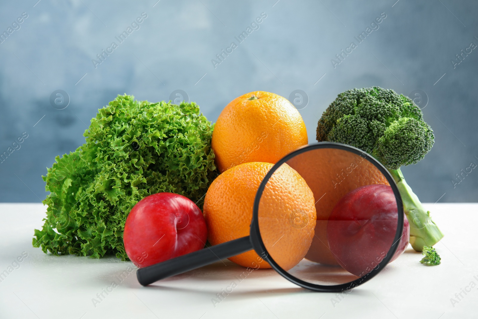 Photo of Fresh fruits, vegetables and magnifying glass on white table against light blue background. Food poisoning concept