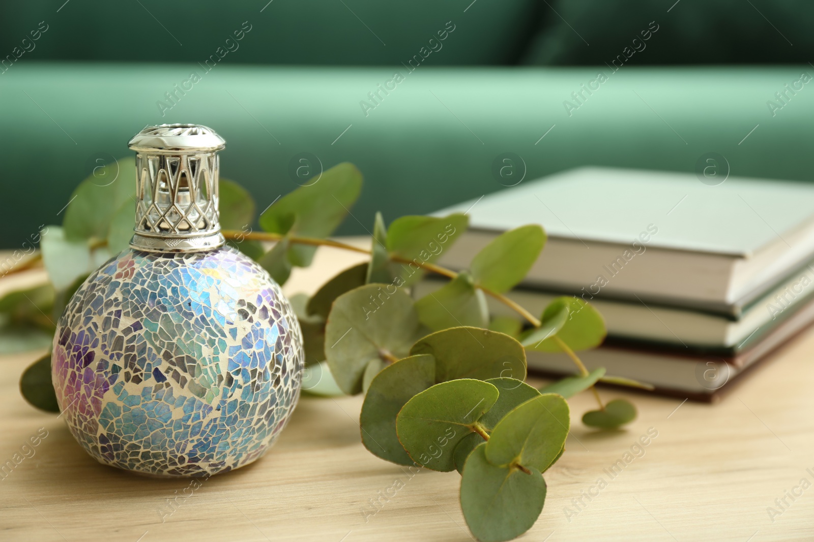 Photo of Stylish catalytic lamp with eucalyptus and books on wooden table in living room, closeup. Cozy interior