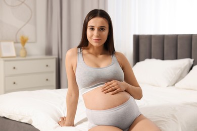 Beautiful pregnant woman in comfortable maternity underwear on bed at home