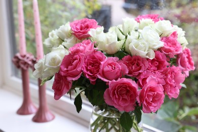 Vase with beautiful bouquet of roses and candles on windowsill indoors, closeup