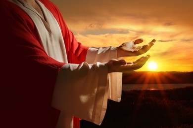 Image of Jesus Christ reaching out his hands and praying at sunset