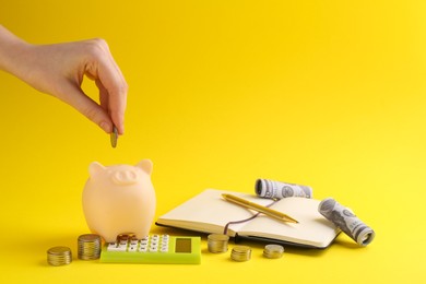 Photo of Financial savings. Woman putting coin into piggy bank on yellow background, closeup