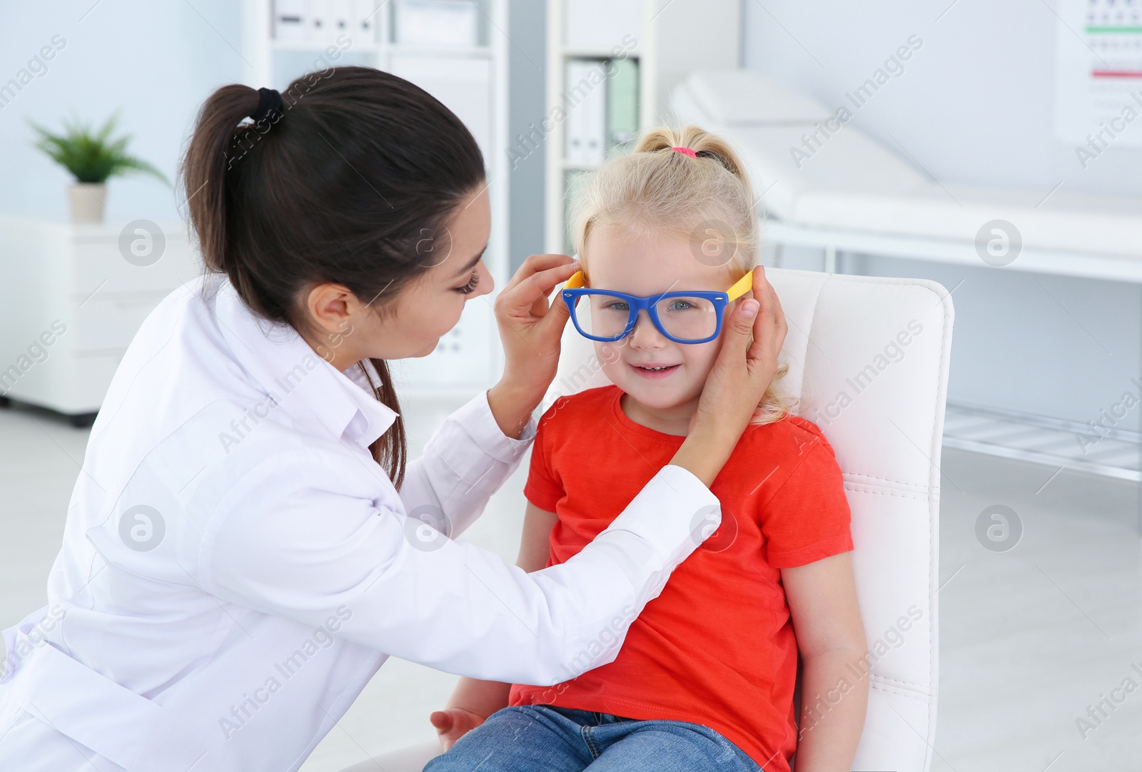 Photo of Children's doctor putting glasses on little girl in clinic