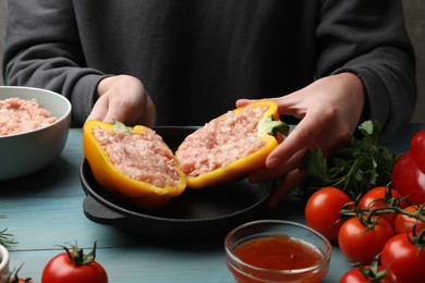 Woman making stuffed peppers with ground meat at light blue wooden table, closeup