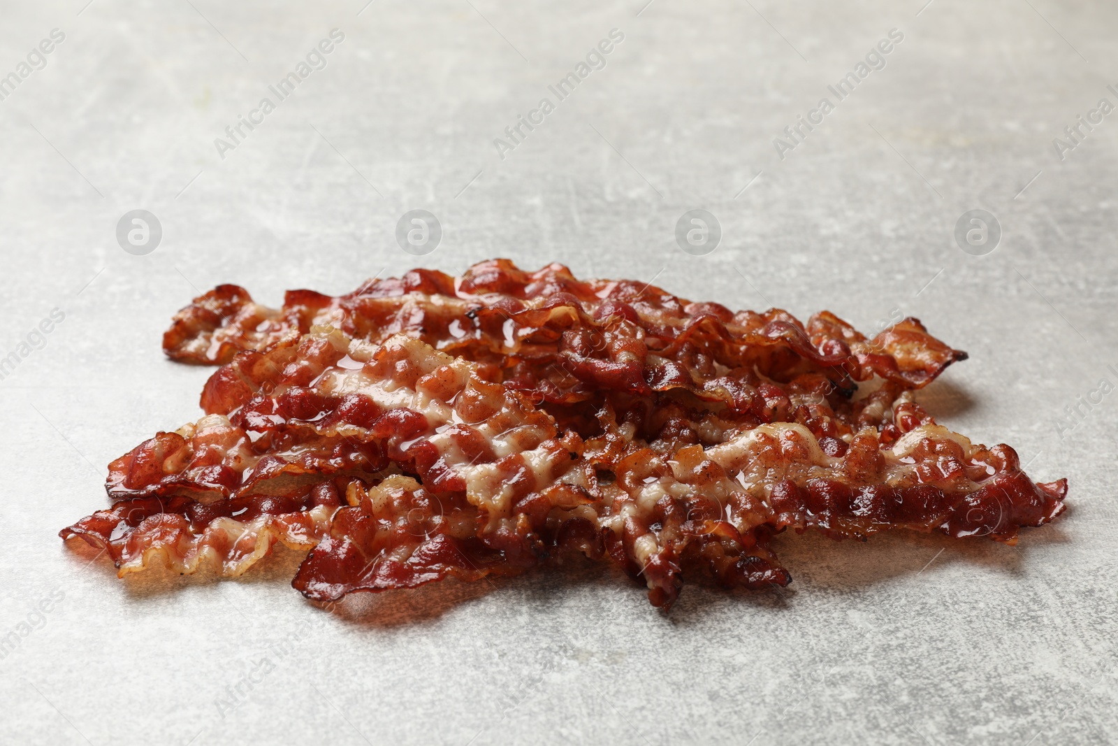 Photo of Pieces of tasty fried bacon on gray textured table, closeup