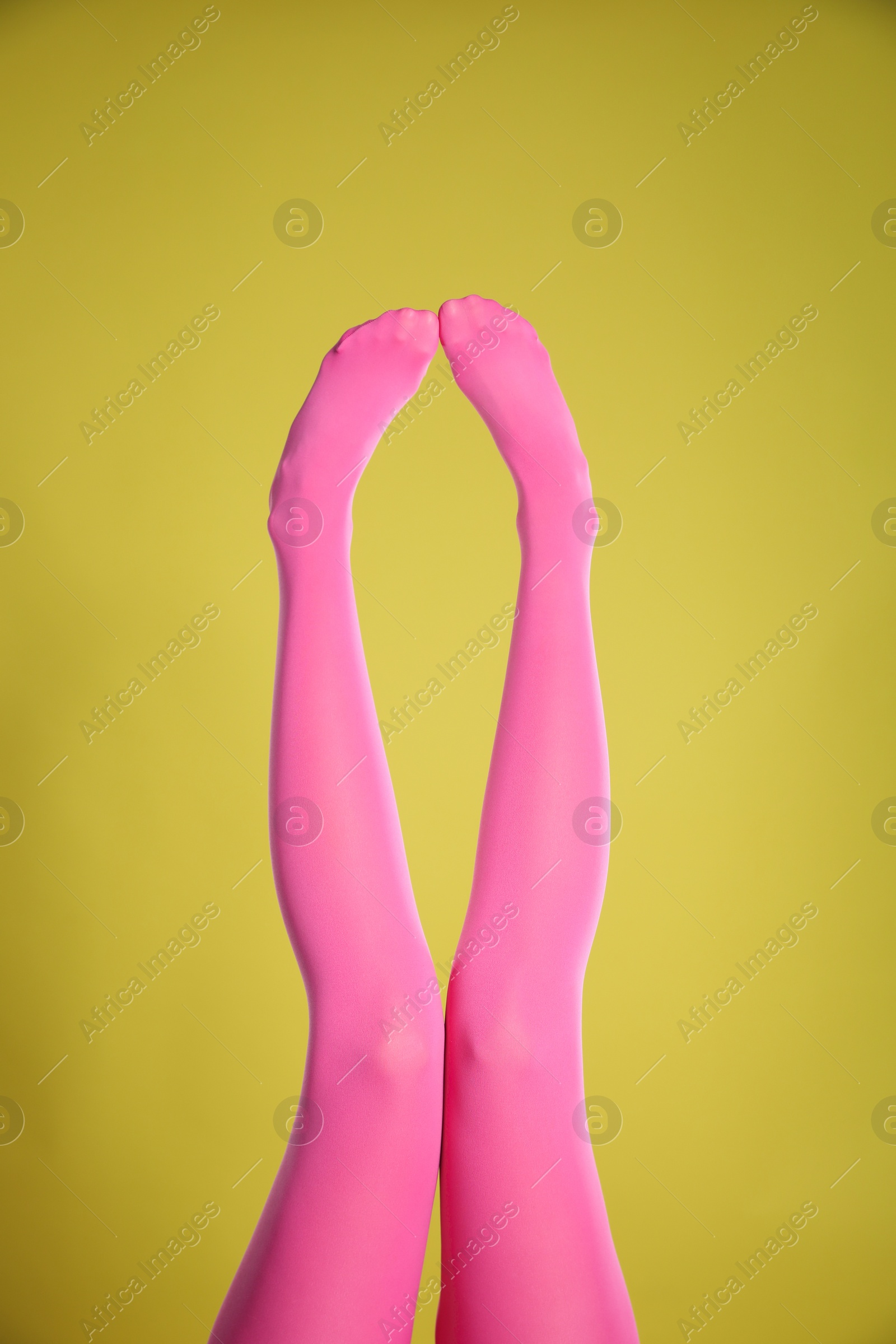 Photo of Woman wearing pink tights on yellow background, closeup of legs