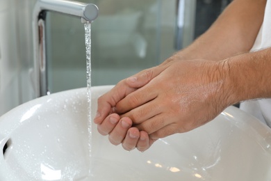 Photo of Man washing hands over sink in bathroom, closeup. Using soap