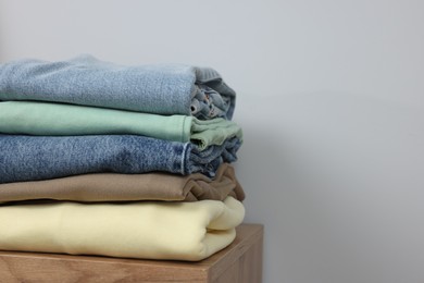 Photo of Stack of different folded clothes on wooden table near grey wall, space for text