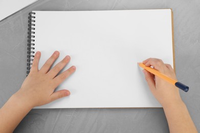 Little boy drawing with pencil at grey textured table, top view. Child`s art