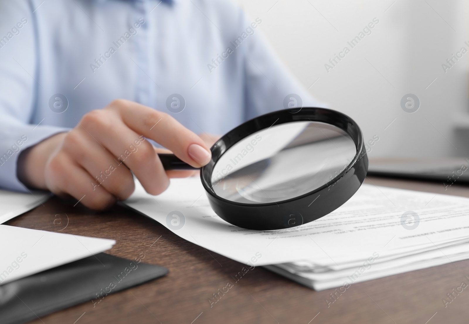 Photo of Woman looking at document through magnifier at wooden table indoors, closeup. Searching concept