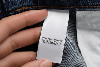Photo of Woman holding clothing label on jeans garment, closeup