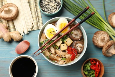 Bowl of delicious ramen and ingredients on light blue wooden table, flat lay. Noodle soup