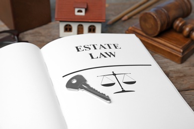 Photo of House key and book with words ESTATE LAW on table, closeup