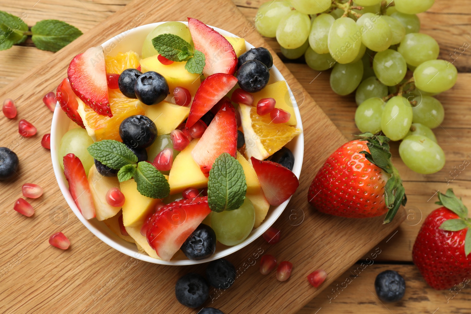 Photo of Tasty fruit salad in bowl and ingredients on wooden table, flat lay