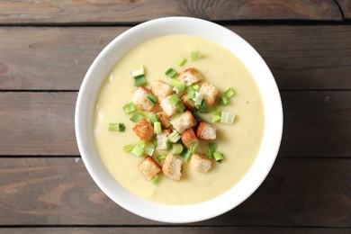 Photo of Tasty potato soup with croutons and green onion in bowl on wooden table, top view