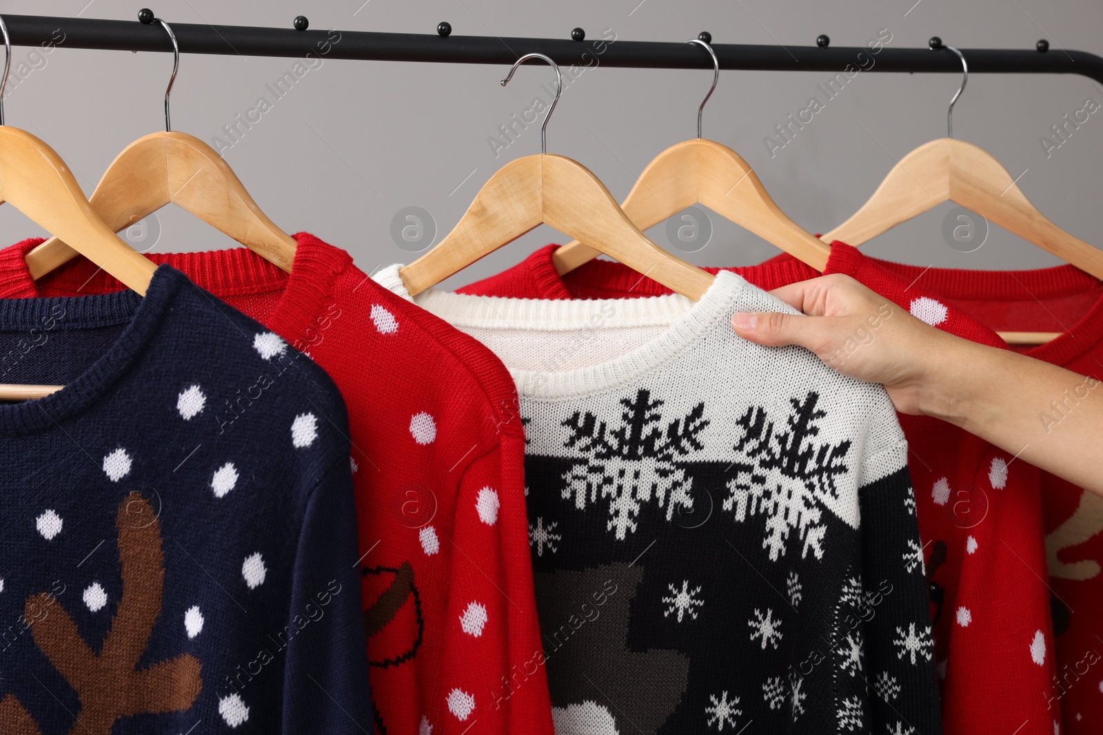 Photo of Woman picking Christmas sweater from rack near light wall, closeup