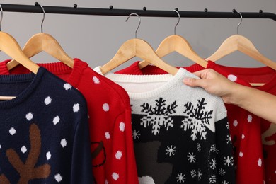 Woman picking Christmas sweater from rack near light wall, closeup