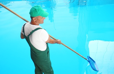 Photo of Male worker cleaning outdoor pool with scoop net