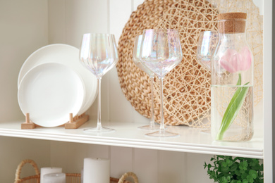 Photo of White shelving unit with glasses, dishes, mats and tulip
