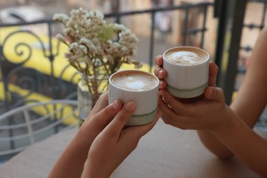 Friends drinking coffee at wooden table in cafe, closeup