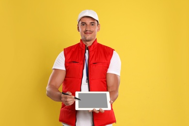 Happy young courier with tablet on yellow background