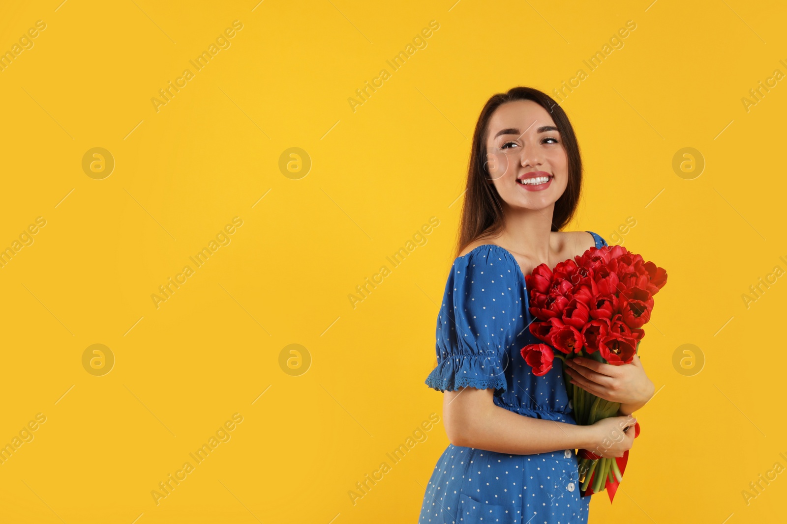 Photo of Happy woman with red tulip bouquet on yellow background, space for text. 8th of March celebration