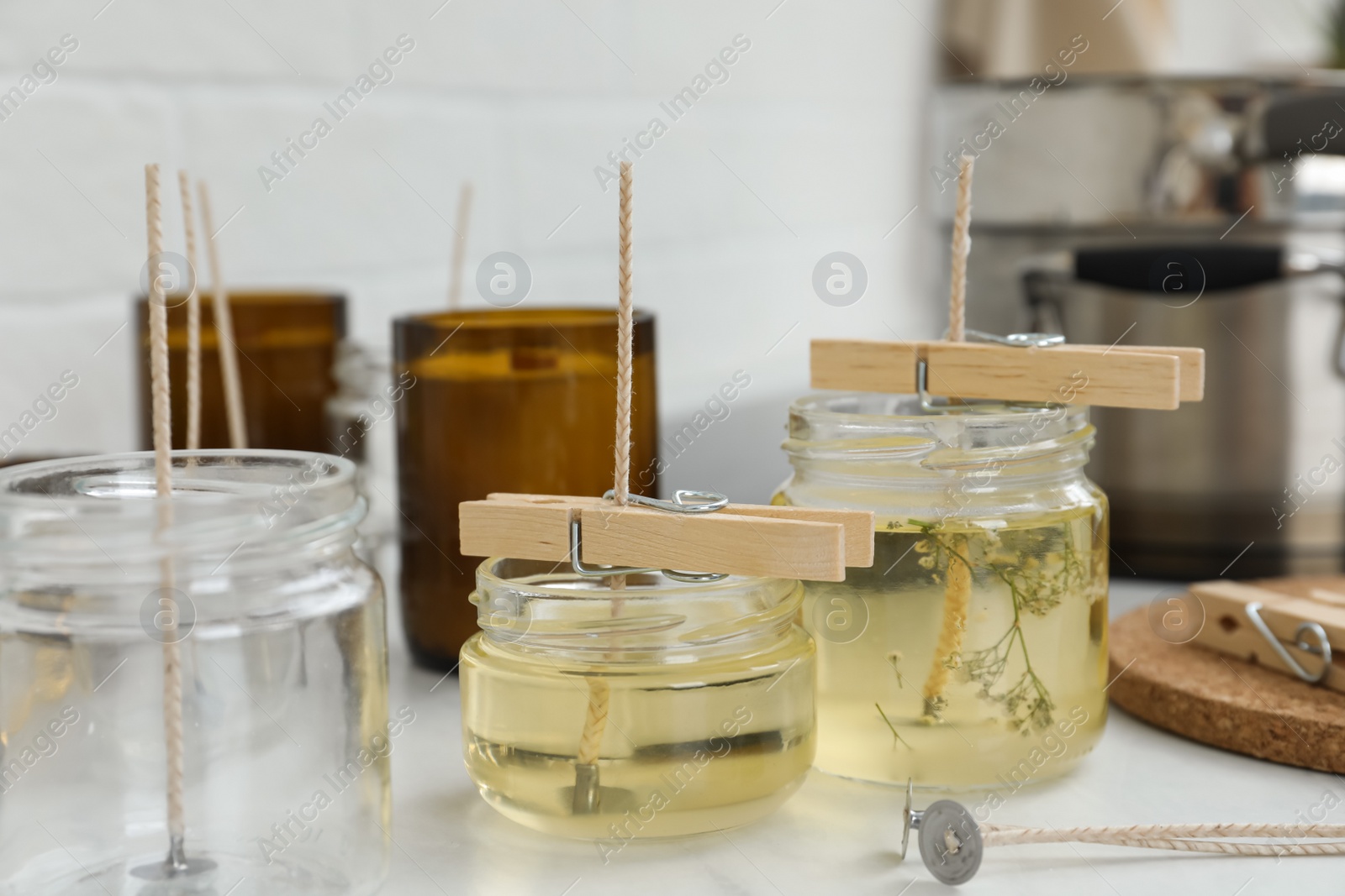 Photo of Glass jars with melted wax on white table. Handmade candles