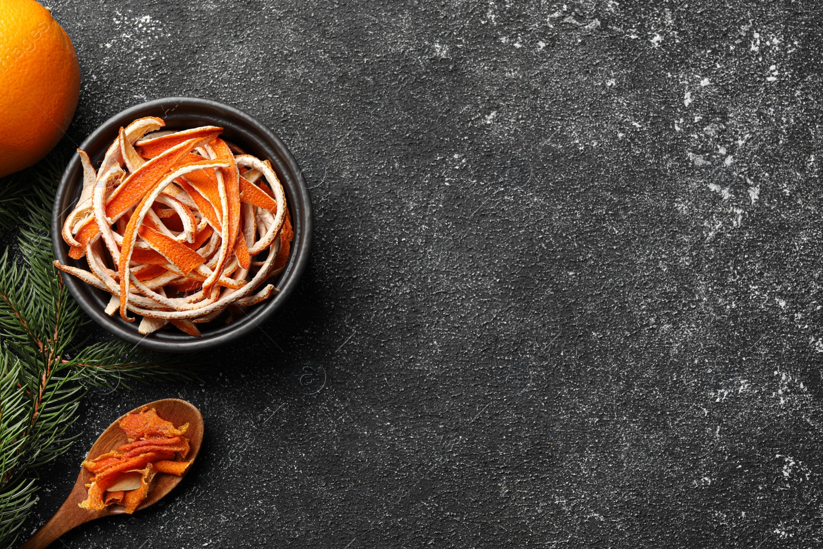 Photo of Dry orange peels and fir branch on gray textured table, space for text