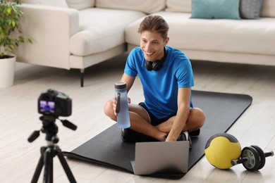 Smiling sports blogger recording fitness lesson with camera at home