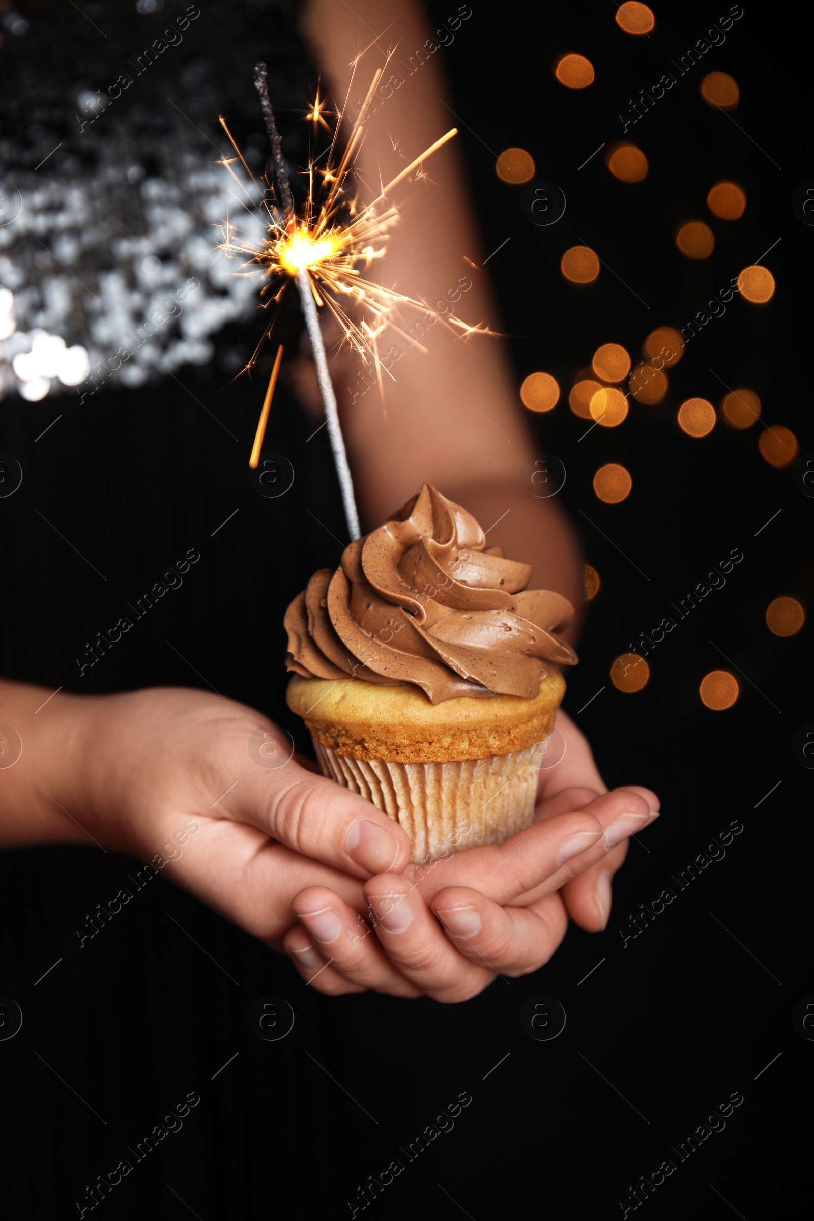 Photo of Woman holding birthday cupcake with sparkler on blurred background, closeup