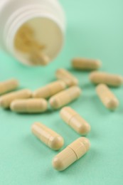 Bottle and vitamin capsules on turquoise background, closeup