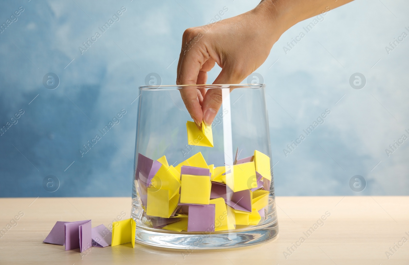 Photo of Woman taking paper piece from glass vase on table. Lottery