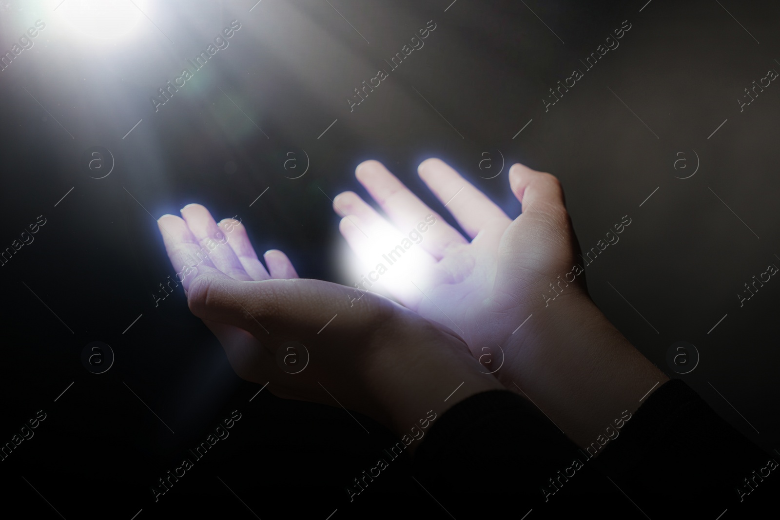 Image of Woman stretching hands towards light in darkness, closeup. Praying concept