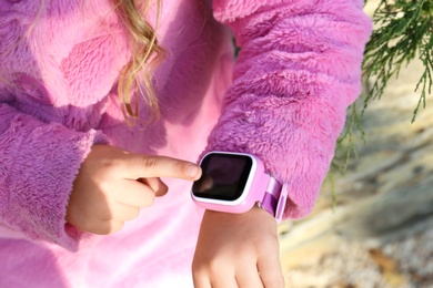 Photo of Little girl using smart watch outdoors, closeup