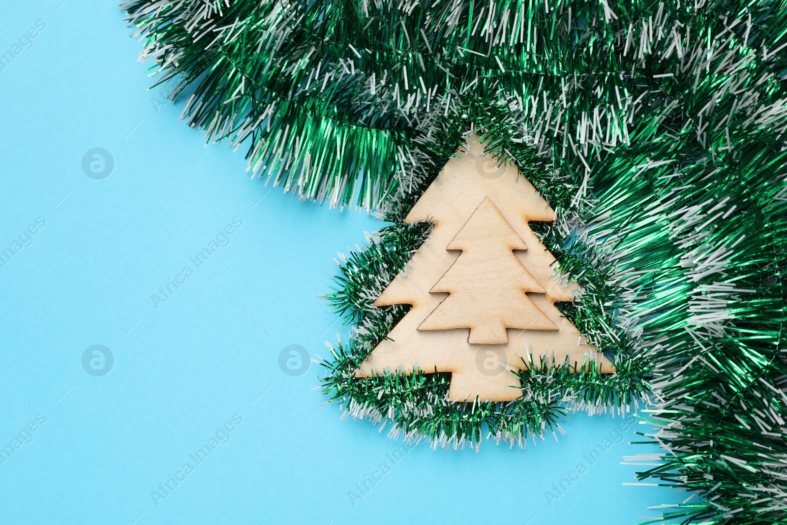 Photo of Green tinsel and Christmas tree toy on light blue background, flat lay. Space for text