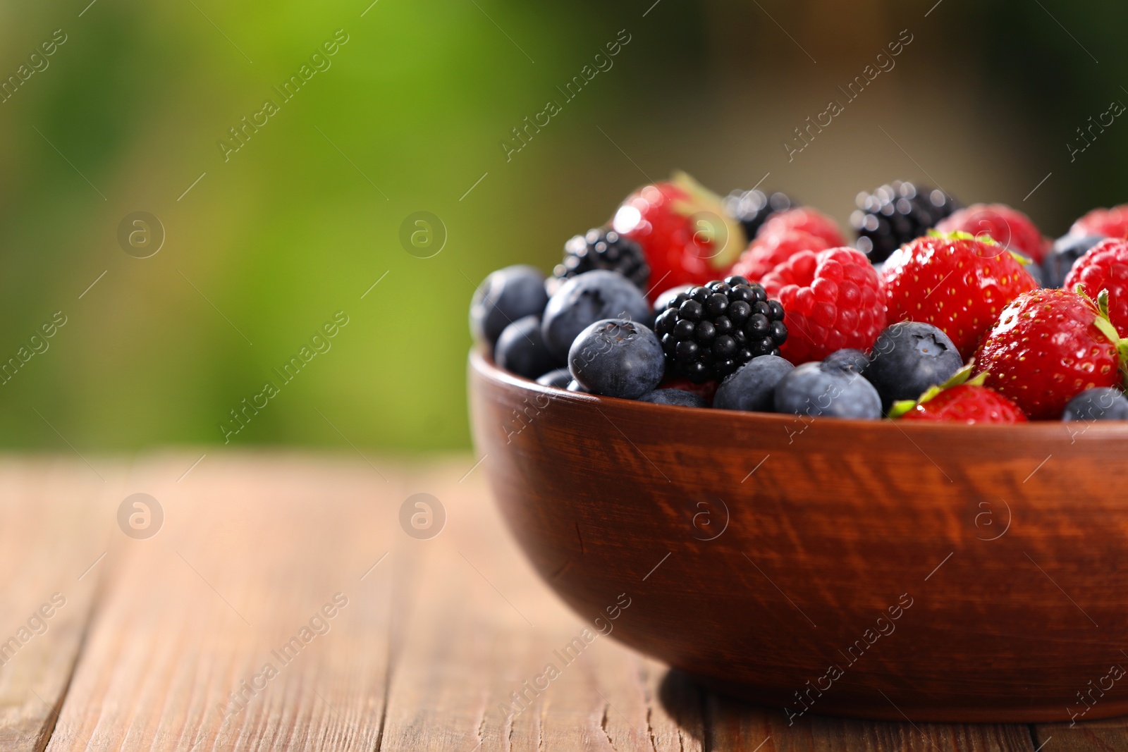 Photo of Bowl with different fresh ripe berries on wooden table outdoors, closeup. Space for text