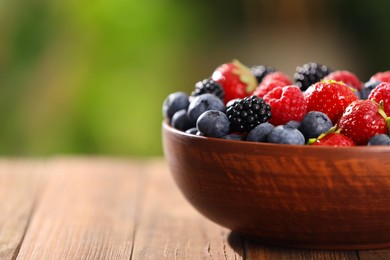 Bowl with different fresh ripe berries on wooden table outdoors, closeup. Space for text