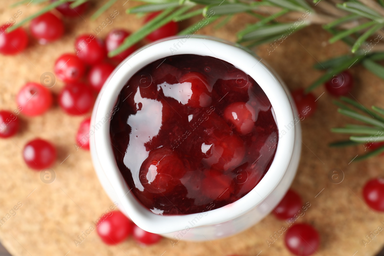 Photo of Cranberry sauce in pitcher, fresh berries and rosemary on board, top view