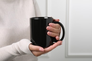 Photo of Woman holding black mug indoors, closeup. Mockup for design