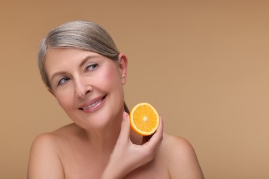 Beautiful woman with half of orange rich in vitamin C on beige background, space for text