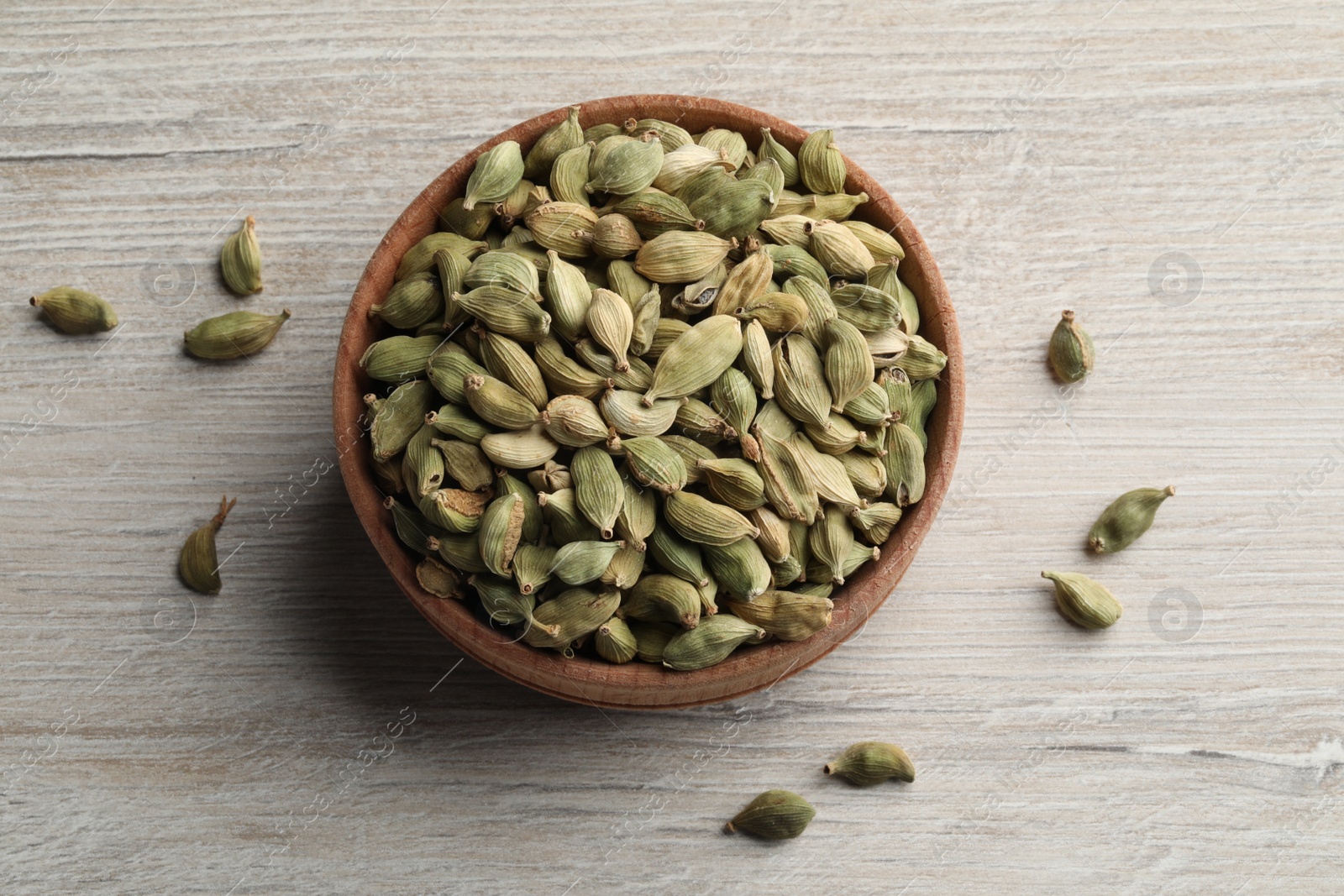 Photo of Bowl of dry cardamom pods on white wooden table, top view