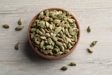 Bowl of dry cardamom pods on white wooden table, top view