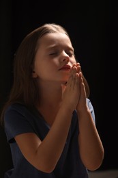 Photo of Cute little girl with hands clasped together praying on black background