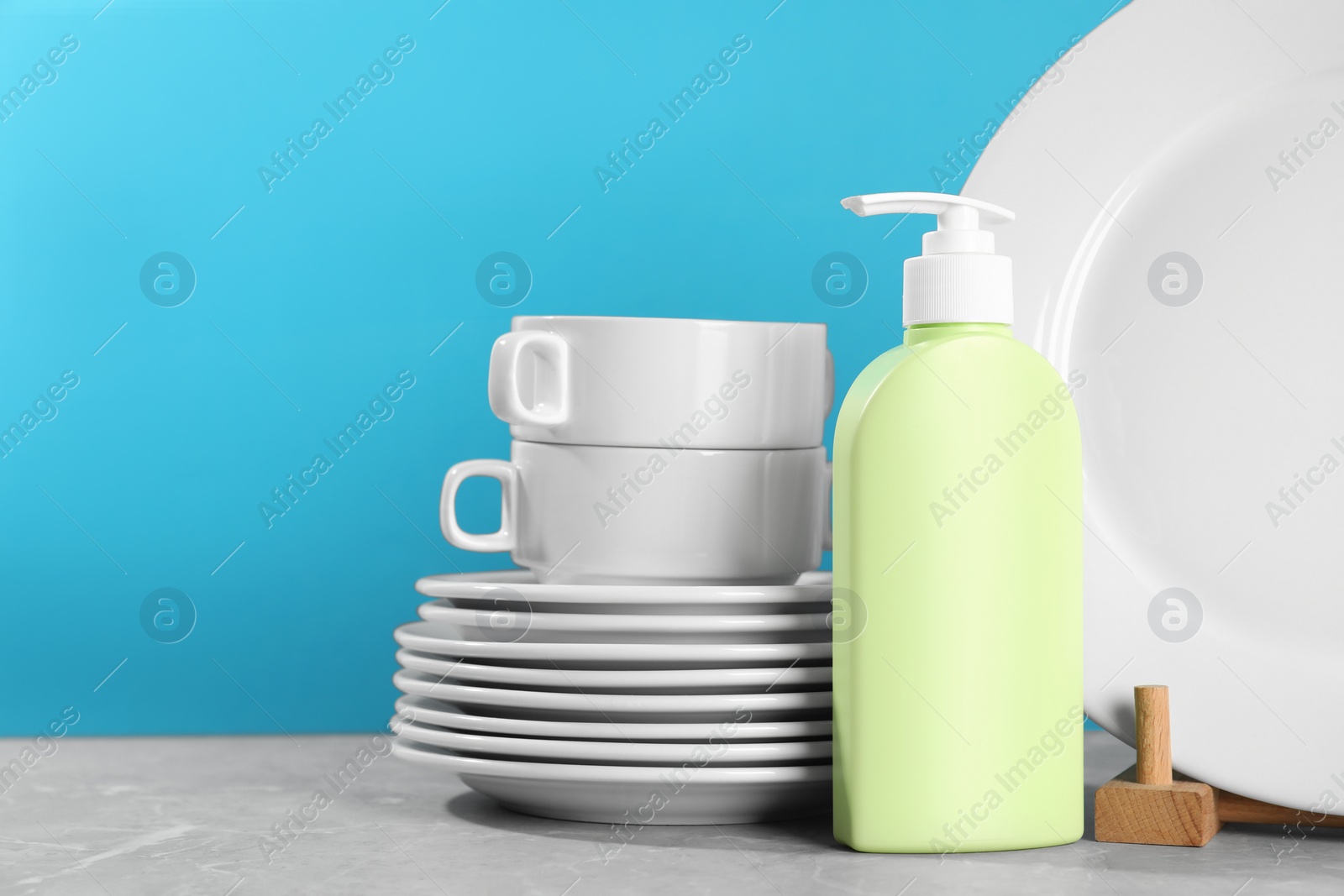 Photo of Set of clean tableware and dish detergent on grey table against light blue background. Space for text